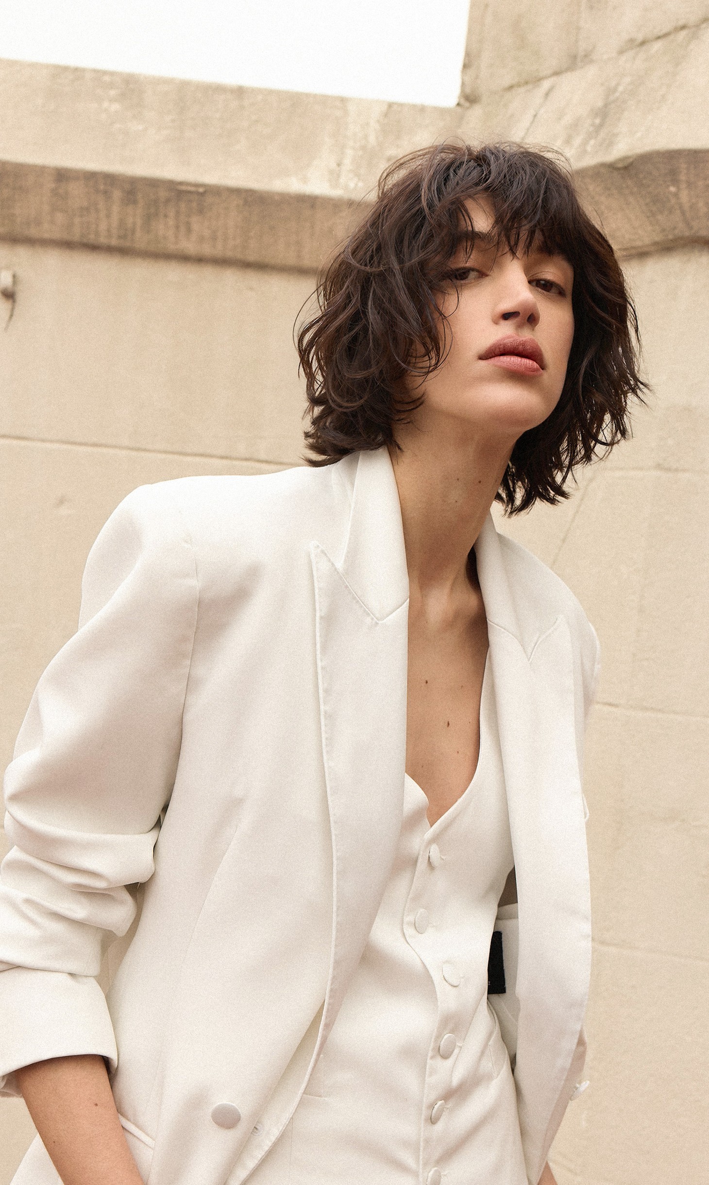 Musa Molten Brunette: melena corta castaña con flequillo y textura, traje sastre blanco.