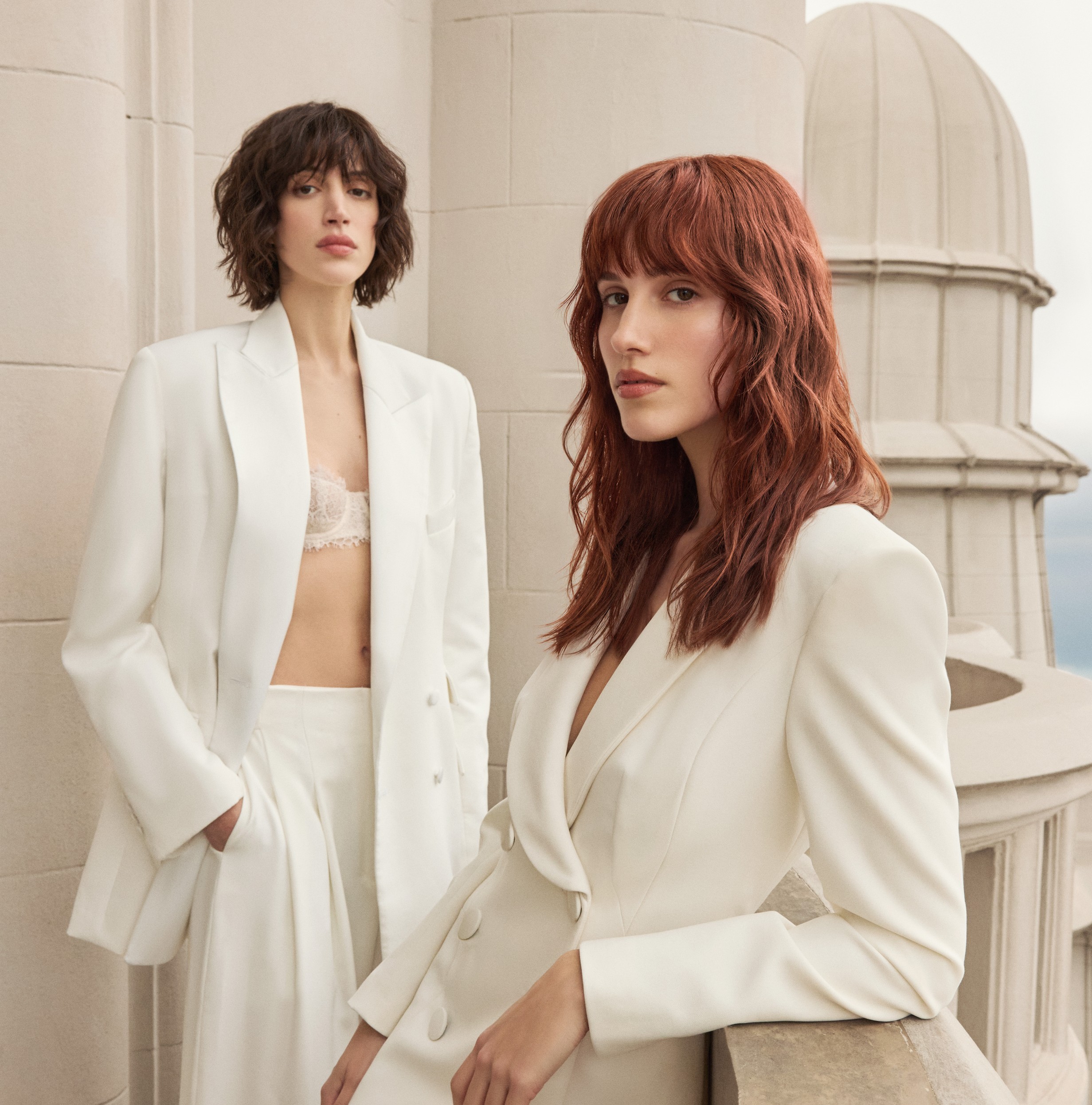 Dos musas de la colección Meridiano con trajes blancos en una terraza de Buenos Aires: una de melena castaña corta y otra de cabello largo cobrizo rojizo.