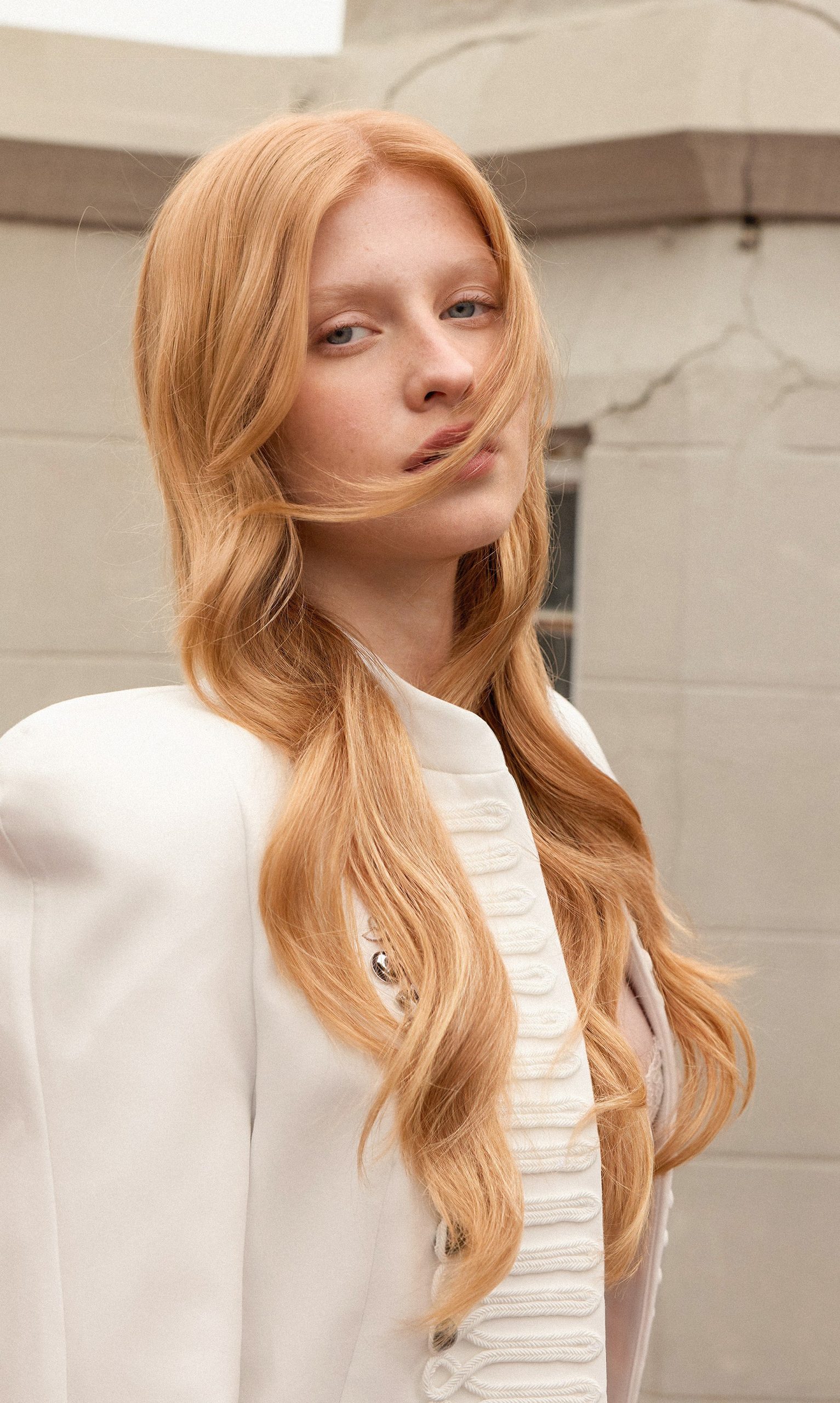 Musa Soft Copper Blonde: cabello muy largo rubio cobrizo movido por el viento, saco blanco.